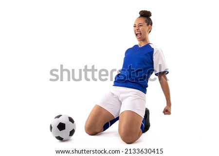Biracial young female soccer player shouting while kneeling by soccer ball against white background. unaltered, sport, sports uniform, copy space, victory, athlete and women's soccer.