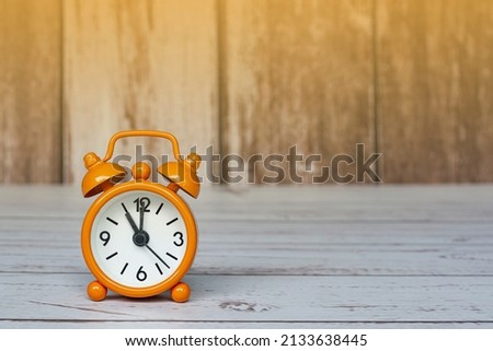 Orange alarm clock isolated on wooden desk. The clock set at 11 o'clock.
