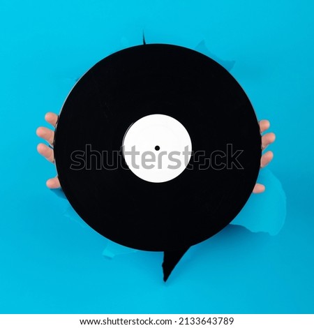 Music, entertainment, technology, retro, vintage concept. Woman hands holding black and blank vinyl record on torn blue paper background with copy space