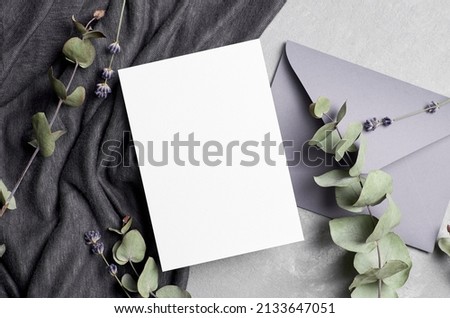 Invitation or greeting card mockup with envelope, eucalyptus and lavender flowers on grey concrete background, top view