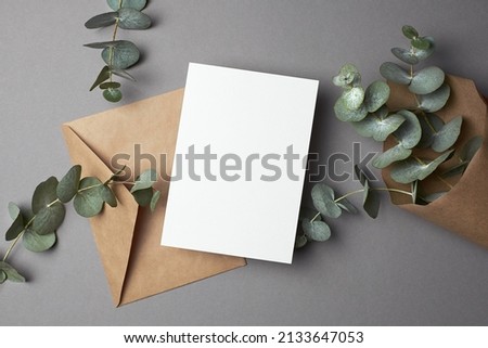 Invitation or greeting card mockup with envelope and natural eucalyptus twigs on paper background. Blank card with copy space.
