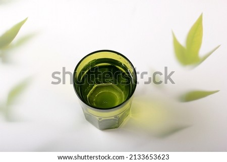 Green glass with water and a light background with plant leaves. Top view green glass of water with sunlight long shadow and refraction patterns and palm leaf trendy shadow 