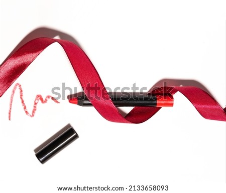 Red matte lipstick in the form of a pencil with red ribbon, smear texture on a white background