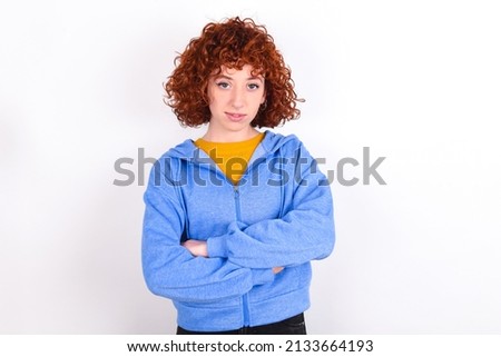Self confident serious calm young redhead girl wearing blue jacket over white background  stands with arms folded. Shows professional vibe stands in assertive pose.