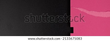 Fragment of a pink notebook with a torn page lying on a black satin background, top view.    