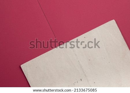 An old, stained piece of paper lying diagonally across the unfolded pink notebook. 