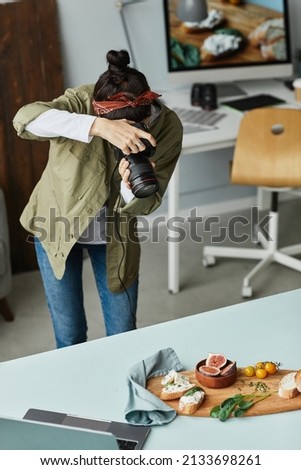 Vertical portrait of female food photographer taking pictures while working in home studio