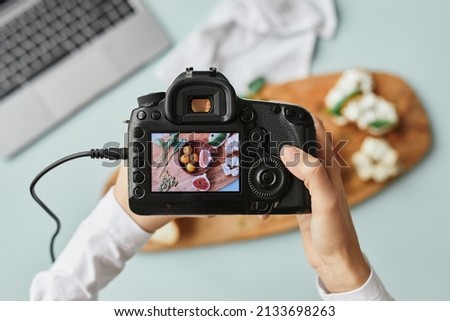 Top view close up of food photographer holding digital camera with image on screen while working in home studio, copy space