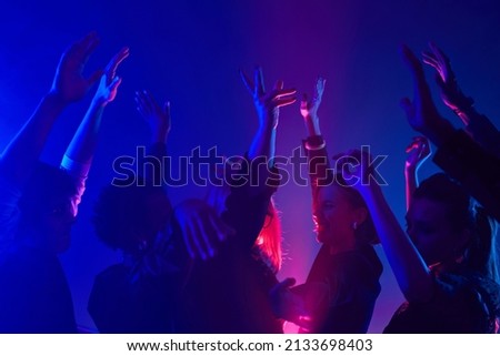 Minimal shot of diverse crowd dancing in club with hands up lit by neon lights Royalty-Free Stock Photo #2133698403