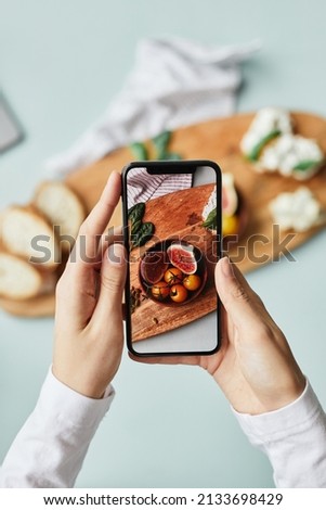 Minimal top view of young woman taking aesthetic photo of food using smartphone in home studio
