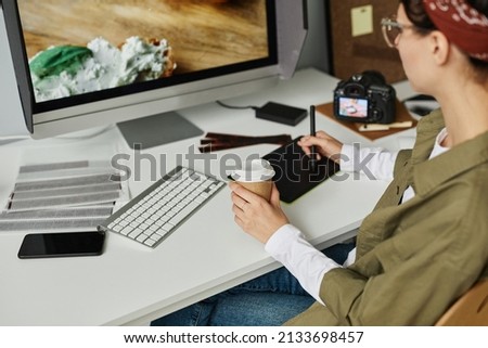 Cropped shot of young female photographer editing pictures at workplace in studio using pen tablet