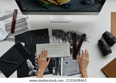 Top view close up of unrecognizable photographer editing photos at workplace in studio, focus on hands using keyboard