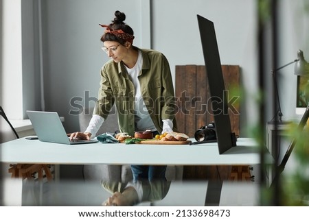 Side view portrait of female food photographer using laptop while setting up scene in studio, copy space