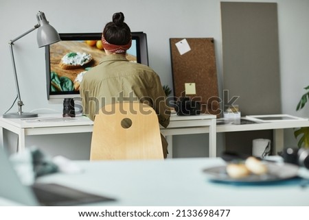 Back view of female food photographer using computer while retouching photos in studio, copy space