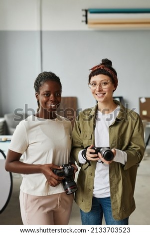 Vertical portrait of two female photographers smiling at camera while standing in photo studio