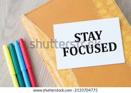 STAY FOCUSED text on a card on a closed notebook on a wooden background