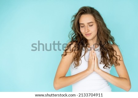 Sincere request. Spiritual woman. Keep calm. Pretty pleading lady holding hands in praying gesture asking favor isolated blue copy space.