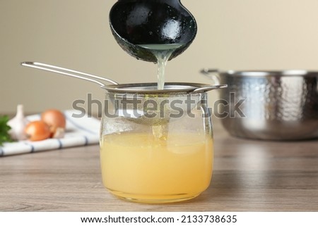 Straining delicious broth through sieve on wooden table
