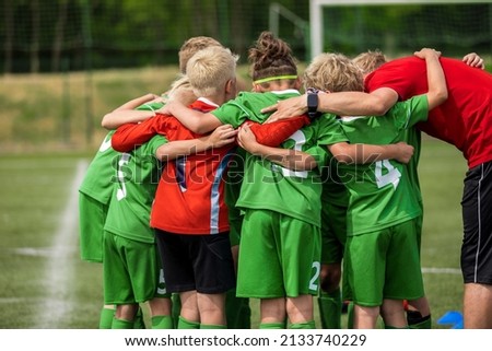 Happy sports team with a young coach. Children playing a football game on stadium pitch. Trainer motivating young players during the pregame briefing. Boys in green soccer jersey uniforms