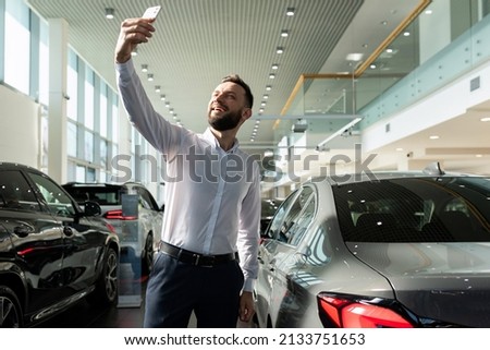 a man takes a picture of himself on the phone in a car dealership against the background of a new car
