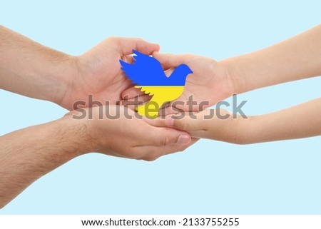 Hands of family with small dove in colors of Ukrainian flag on light background. War in Ukraine