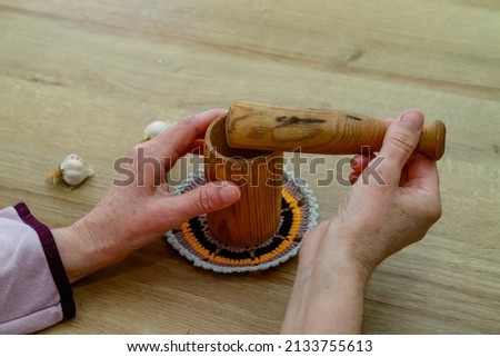 woman is holding a wooden crushed garlic grinder on the table. Fresh garlic. Royalty-Free Stock Photo #2133755613