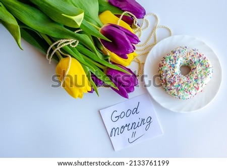 A note with the inscription "Good morning", a bouquet of flowers and a donut on a light background