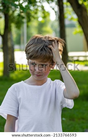 The child scratches his head. A boy with long thick hair has an itchy head due to dandruff. 