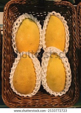 A picture of ripe Nam Dok Mai mangoes is placed on a basket.