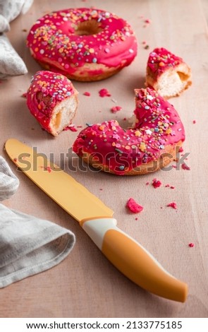 round donuts with pink icing on a wooden board, a knife and a cotton napkin lie nearby. Bright arrangement of sweets