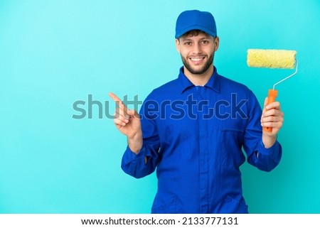 Painter caucasian man isolated on blue background pointing to the side to present a product