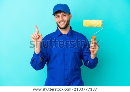 Painter caucasian man isolated on blue background showing and lifting a finger in sign of the best