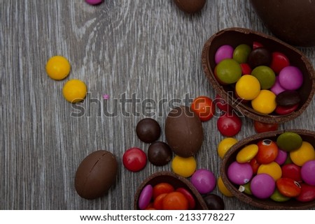 Food photography with chocolate eggs and multi-colored round candies on a dark wooden background. Photo for Happy Easter. Top view