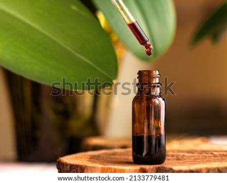 a drop of serum with a pipette drips over a brown glass jar on green background close-up. selective focus. beauty concept. natural cosmetic. Daily skin care. Anti-aging serum with natural ingredients Royalty-Free Stock Photo #2133779481