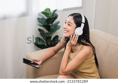 Relaxing time in living room. Beautiful young asian woman choose music from smartphone take a rest and listening song with headphone. Lifestyle in living room at house in the morning.