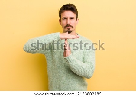 young hispanic man looking serious, stern, angry and displeased, making time out sign
