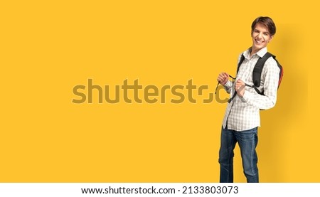 Young male student with backpack posing on background