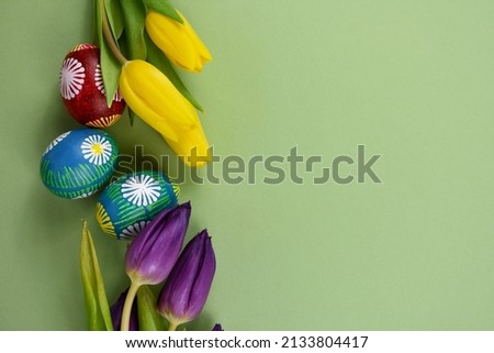 Beautiful hand painted easter eggs with yellow and purple tulips frame stock images. Easter colored eggs isolated on a green background with copy space for text stock photo. Unique easter eggs border