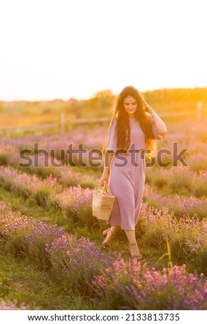 Portrait of stylish beautiful female walking at the lavender field, relaxing from city life. Brunette woman with picnic basket spending weekends outdoors, enjoying fresh air, beautiful nature concept.