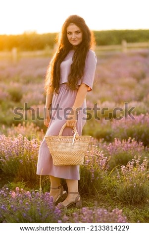 Happy portrait of stylish gorgeous female walking at the field, posing, looking at the camera. Brunette woman with picnic basket spending weekends outdoors, beautiful nature concept.
