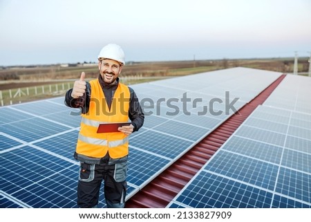 Portrait of a worker using tablet to check on solar panels and giving thumbs up for passing the test.