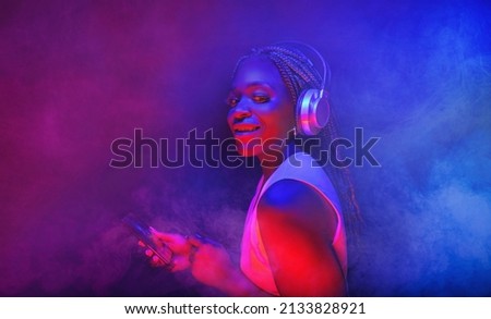  Young African American woman wearing headphones listening to music and dancing in futuristic purple cyberpunk neon light background 