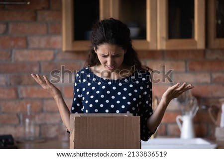 Unhappy anxious young latin woman unboxing carton parcel, dissatisfied with wrong item or smashed order, disappointed with low quality delivery service, negative online shopping experience concept. Royalty-Free Stock Photo #2133836519