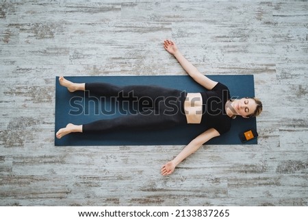 A beautiful blonde girl does yoga lying on the floor. Relaxing the muscles of the body and selfcare.Shavasana.Practice yoga at home. High quality photo Royalty-Free Stock Photo #2133837265