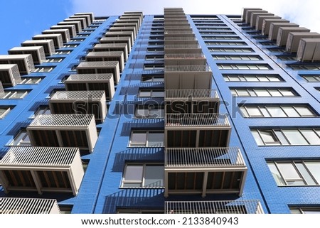 A city urban image of a large blue tower block rising towards the sky.  Balconies are on each floor and form a regular pattern.