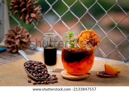 A glass of iced Americano black coffee and a layer of orange juice and lemon are decorated with coffee beans.
