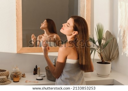 A beautiful young woman sprays perfume on her neck while standing in the bathroom. Royalty-Free Stock Photo #2133853253