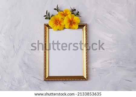 Flat lay with empty golden photo frame and yellow primrose flowers on concrete background. Top view, copy space. Template for branding and advertising