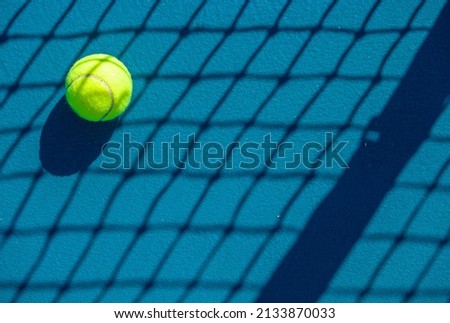 close-up of a tennis ball lying on a hard blue court in the shadow of a tennis net Royalty-Free Stock Photo #2133870033