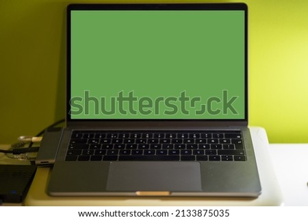Computer with green screen standing on desk in front of yellow background
